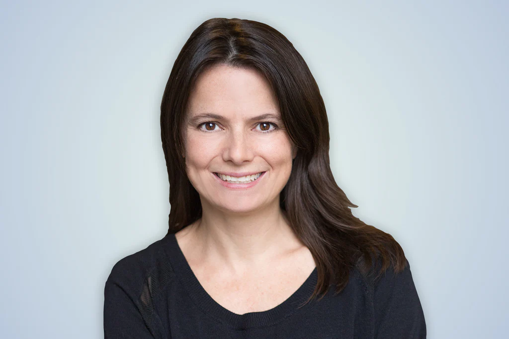 female with brown hair and brown eyes. Wearing a black shirt. her name is Amy Hood and the background is a gray.