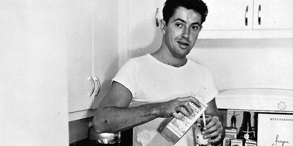 An old image of Lou Rand Hogan, a man with brown hair wearing a plain white t-shirt, pouring milk into a glass