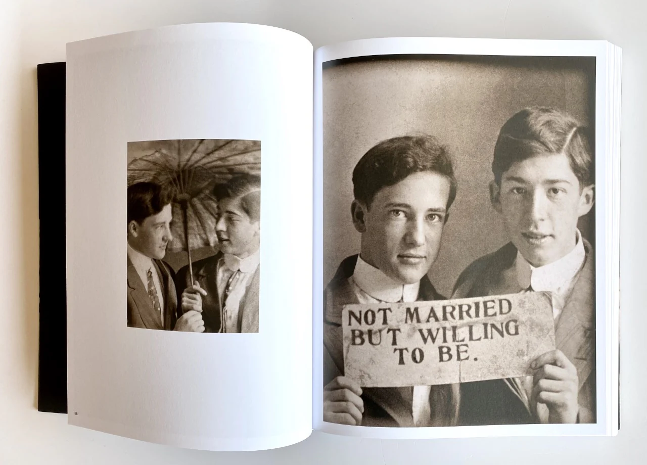 A photo of a spread from Loving: A Photographic History of Men in love, 1850s-1950s. On the left, there is a photograph of two men looking at each other under an umbrella. On the right, there are two men looking at the camera and holding a sign that says "Not married but willing to be." In all capital letters.