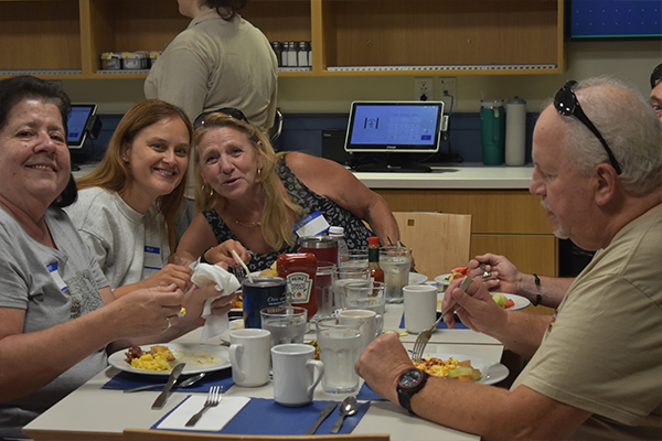 Three women smiling for a photo while sitting at a table and eating.