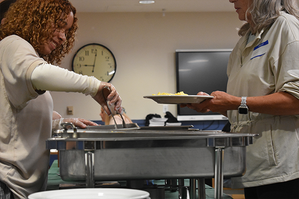 A girl serving eggs out of a metal heating tray to a woman.