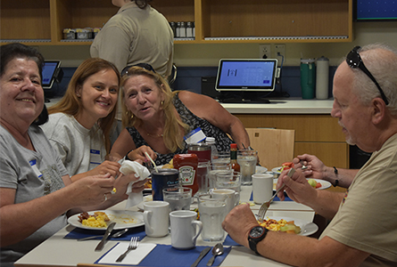 Three women smiling for a photo while sitting at a table and eating.