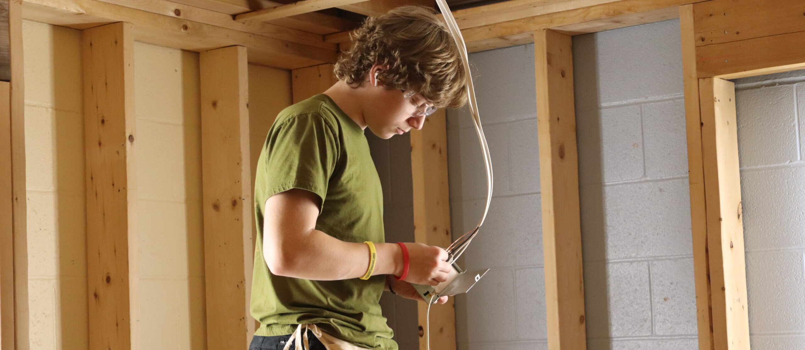 A student on a ladder adjusting the wiring in an overhead light inside of a house.