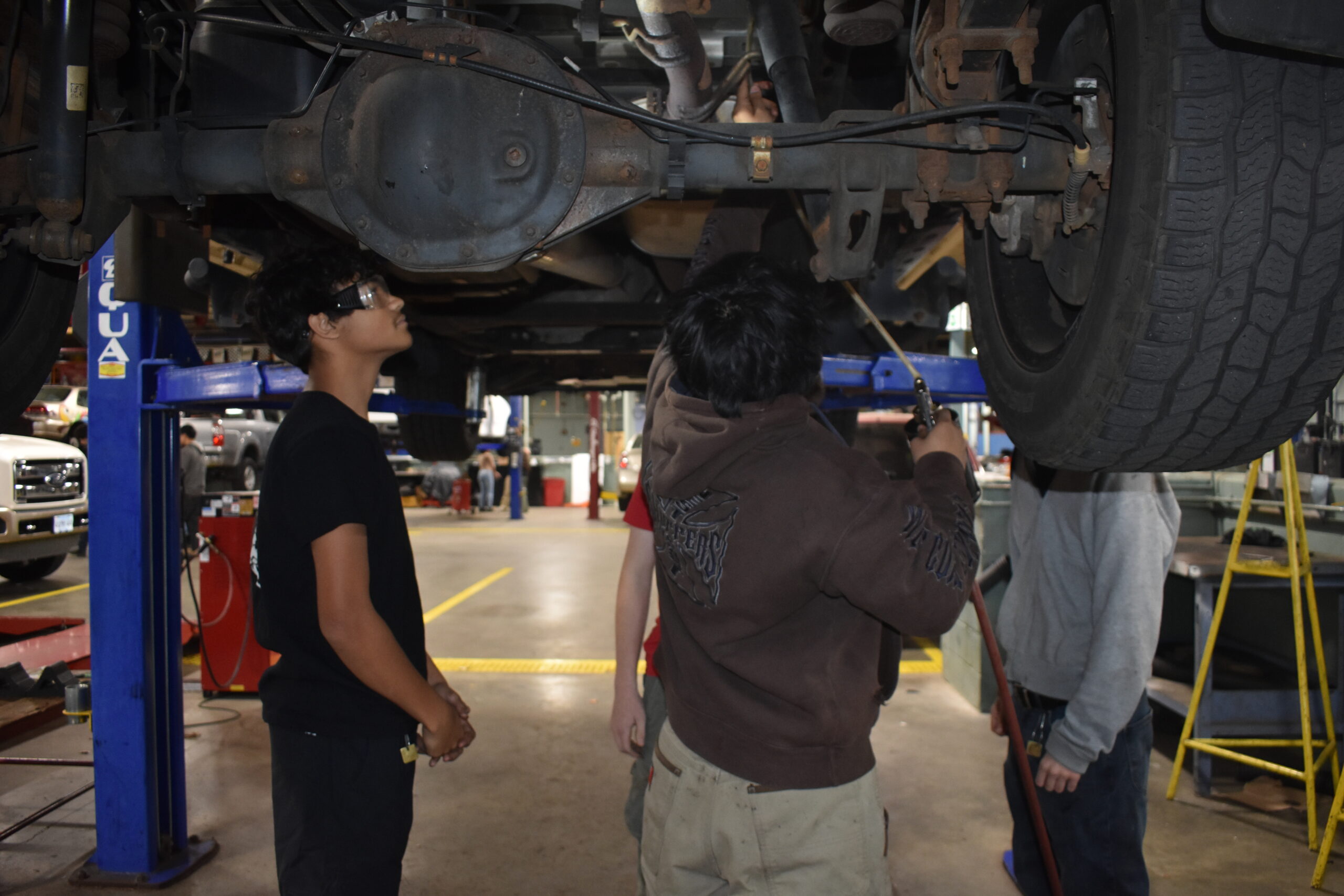  students looking up a lifted car and fixing somethin