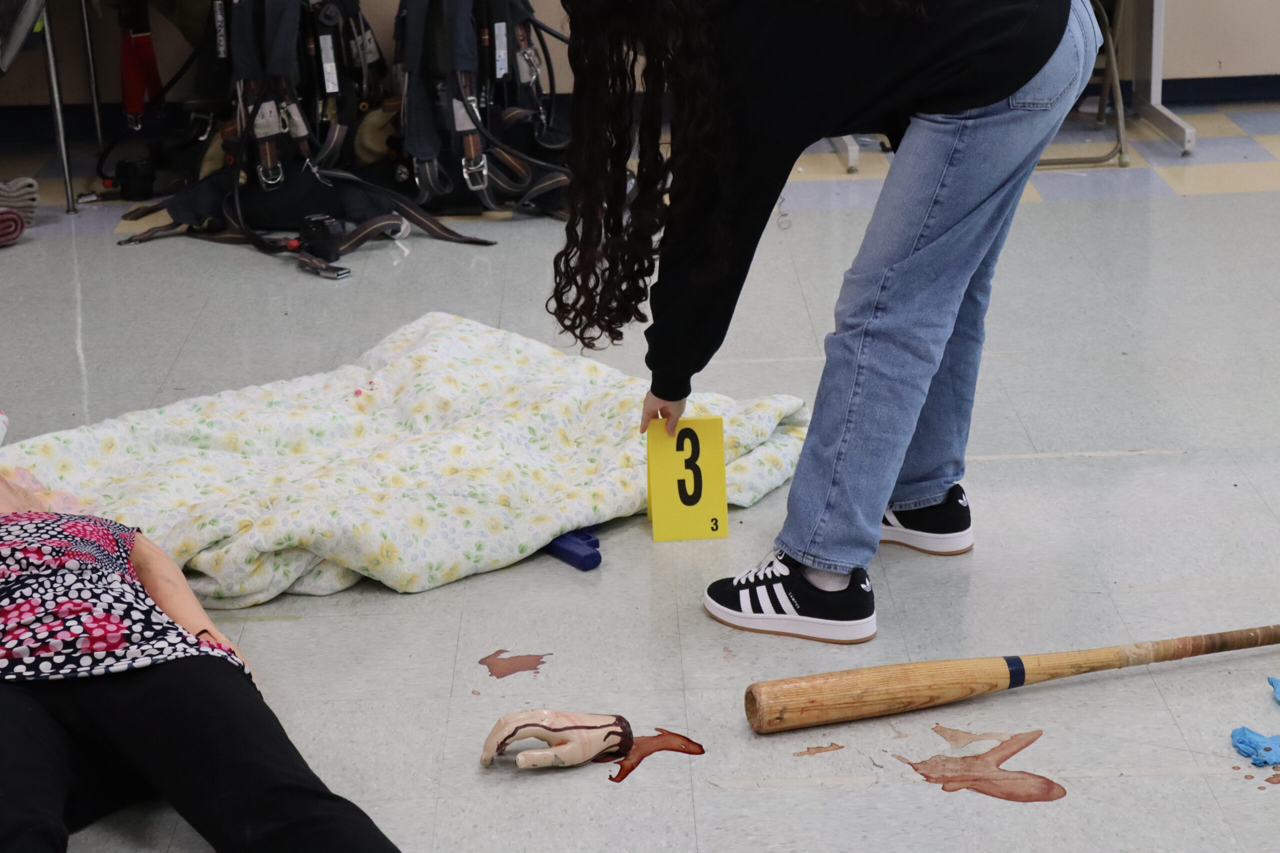 A student placing down a photo evidence marker on a piece of evidence at a fake crime scene.