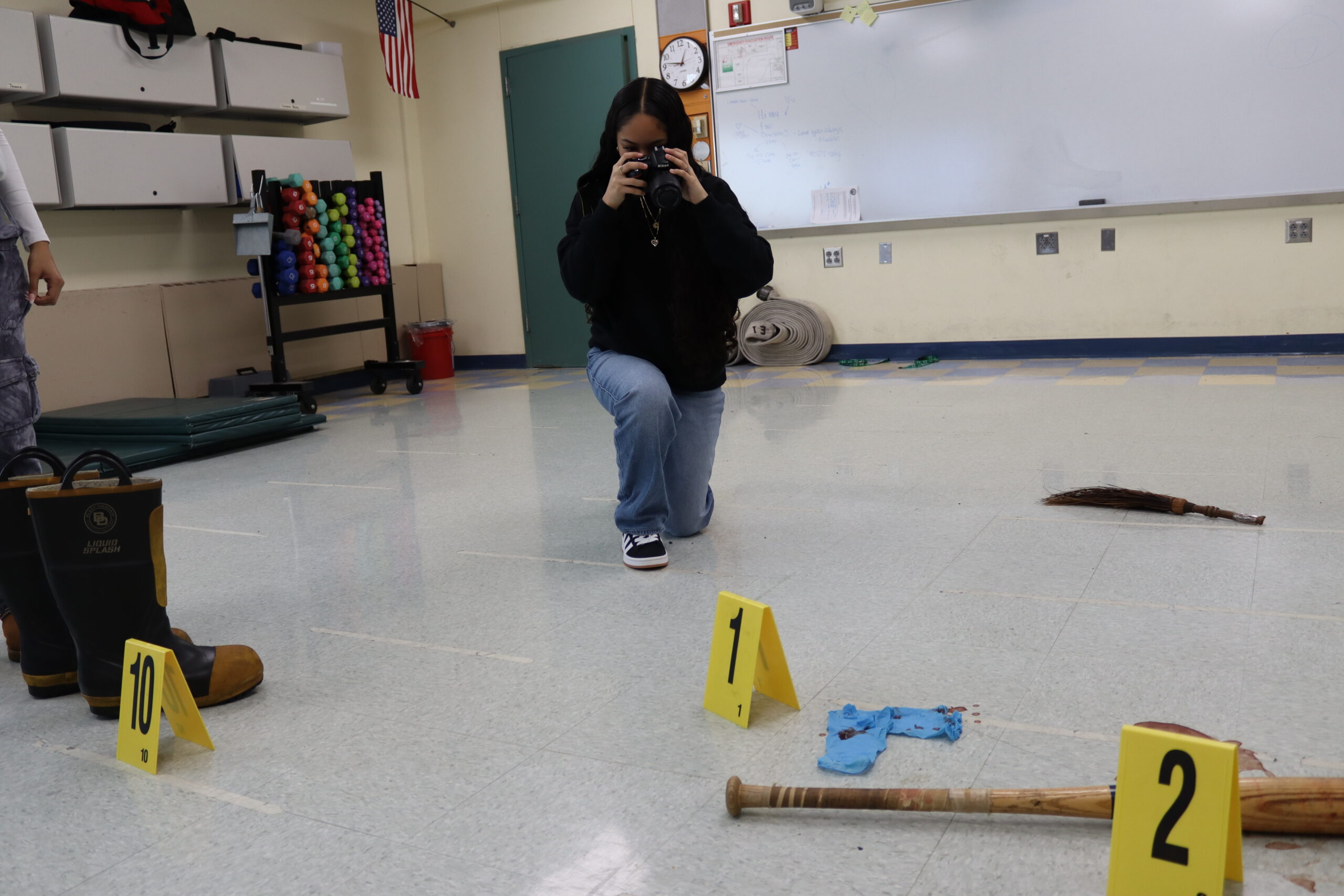 A student crouched down taking a photo of the evidence in a fake crime scene using a professional camera. 