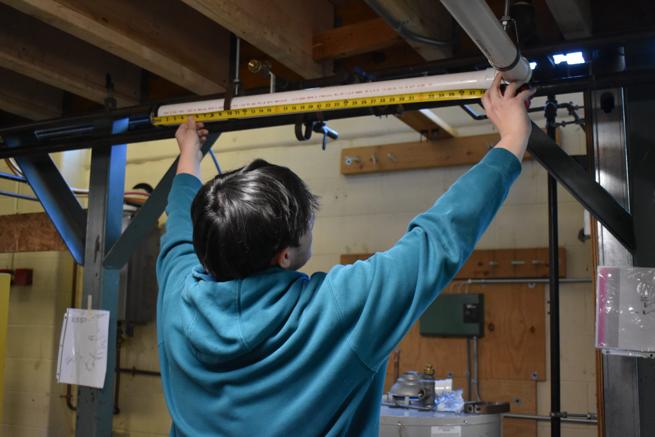 Student using measuring tape to measure a drain pipe<br />
